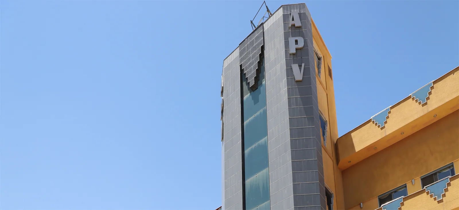 APV Group headquarters in Damascus at dusk: a grey stone tower with vertical APV letters beside an ochre wing